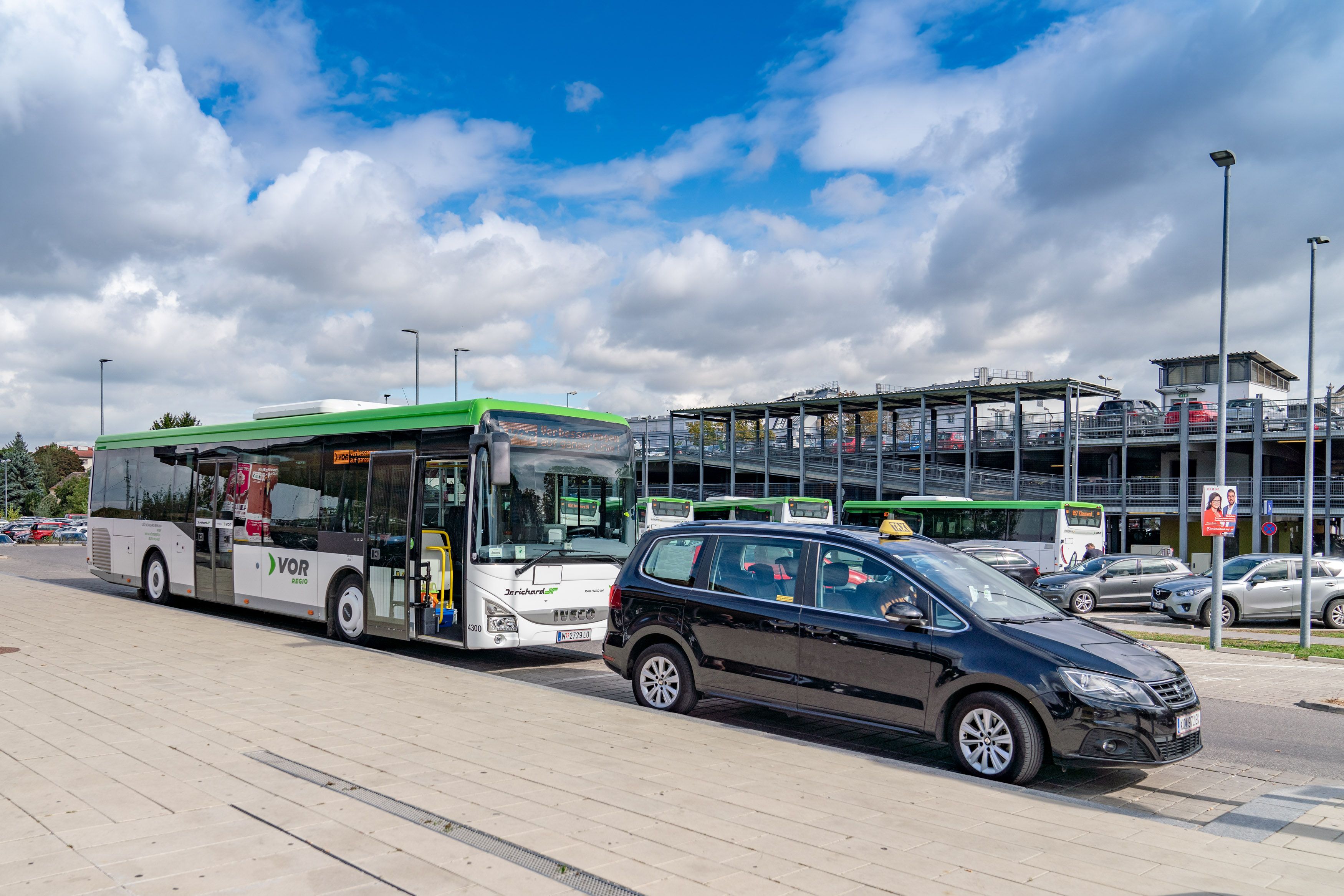 chwarzes Anrufsammeltaxi vor einem Regionalbus an einem Busterminal.  